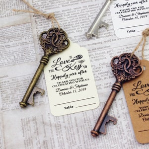 May include: Two antique-style skeleton keys with bottle opener features. Each key is attached to a tag with the text "Love is the key to happily ever after" and the text "Thank you for celebrating with us Dominic & Stephanie October 15, 2019".