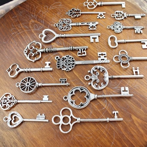 May include: A collection of 18 antique-style silver keys with intricate designs. The keys are arranged on a wooden surface.