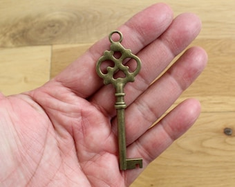May include: A decorative antique-style key with an ornate design, made of brass and featuring a keyhole and a loop at the top.