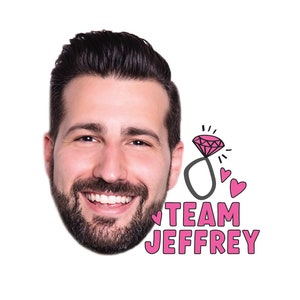 May include: A pink and white printable party sign with a cartoon drawing of a ring with a diamond and two hearts. The text on the sign reads "Team Jeffrey".