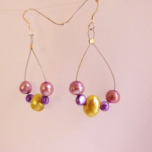 May include: A pair of dangle earrings with a silver wire and a cluster of purple and gold beads.