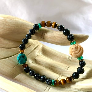 May include: Black and brown beaded bracelet with a carved wooden charm, turquoise beads, and green accents.