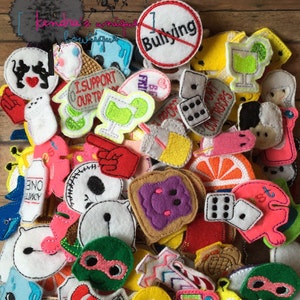 May include: A collection of colorful felt appliques in various shapes, including a stop sign with "Bullying" crossed out, dice, and cartoon characters. The appliques are scattered on a wooden surface.