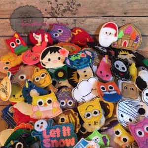 May include: A collection of colorful felt ornaments in various shapes, including owls, characters, and holiday-themed designs. The ornaments are in shades of red, blue, yellow, and pink, with embroidered details and the text "Let It Snow".