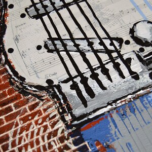 K&ouml;nnte beinhalten: Nahaufnahme eines Gitarren-Kunstwerks. Das Gem&auml;lde zeigt einen Gitarrenkorpus mit schwarzen Saiten, wei&szlig;en Stimmwirbeln und einem Hintergrund aus Notenbl&auml;ttern. Eine Backsteinmauer und blaue Akzente setzen Kontraste.