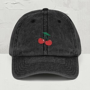 May include: A black vintage washed denim baseball cap with a red cherry embroidery.