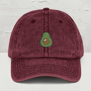 May include: A maroon vintage washed cotton baseball cap with an embroidered avocado design.