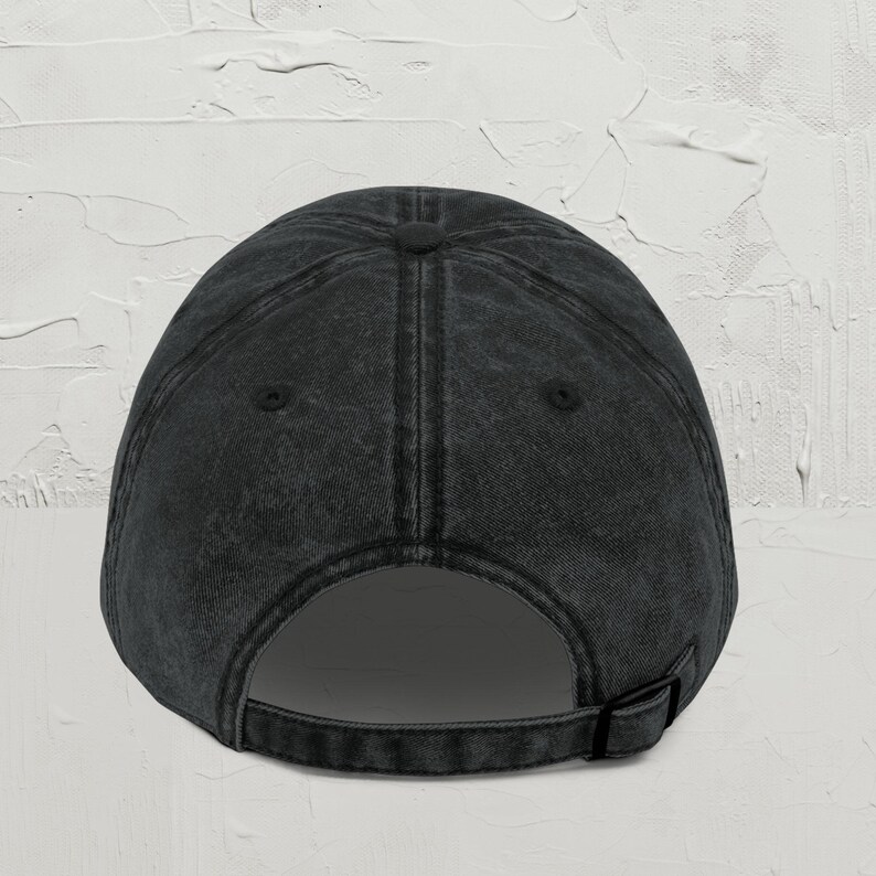 May include: A dark gray baseball cap with a curved brim and adjustable strap. The cap has a vintage, worn look, with visible stitching and a button on top. The back features an adjustable strap for a custom fit.