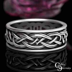 May include: A silver-toned ring featuring an intricate, continuous woven knot pattern around the band. The metal surface has polished highlights and darkened recessed areas. The text Celtic Eternity is visible in the bottom right corner.