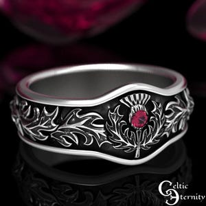Puede incluir: Un anillo de plata con acabado de esmalte negro presenta un diseño detallado de nudo celta y una piedra preciosa roja en el centro. El anillo es un símbolo tradicional de fuerza y unidad.