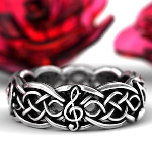 May include: A silver ring with a Celtic knot design featuring a treble clef in the center.