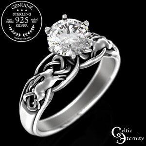 May include: Sterling silver Celtic knot ring with a large round cubic zirconia stone. The ring features a detailed design of two intertwined knots with a hare or rabbit in the center.