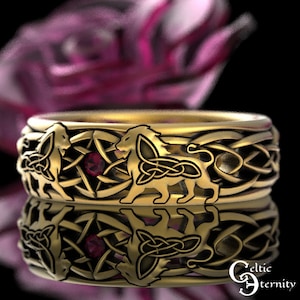 May include: A gold ring with a Celtic knot design featuring two lions and a red gemstone. The ring is set against a blurred background of pink flowers.