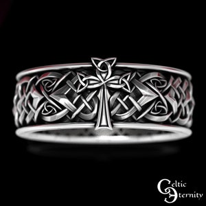 May include: Silver Celtic knot ring with a cross design. The ring is intricately detailed and features a Celtic knot pattern.
