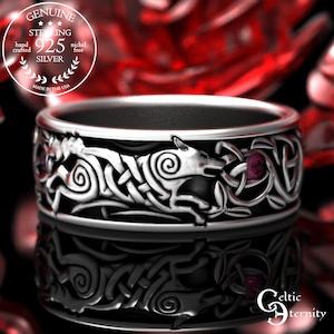 May include: A sterling silver ring with a black interior and a detailed wolf and Celtic knot design. The ring features a polished finish and a small, round, red gemstone. The ring is nickel-free and hand-crafted in the USA.