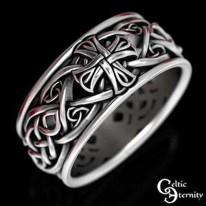 May include: A silver-toned ring featuring an intricate, raised relief pattern of interwoven knots and a central cross motif. The band has a smooth, polished interior surface and a textured, detailed exterior. The text Celtic Eternity is visible.