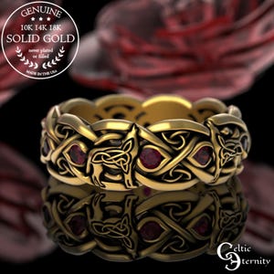 May include: A gold Celtic knot ring with red gemstones. The ring is made of 10K, 14K, or 18K solid gold and is made in the USA. The ring features a Celtic knot design with a wolf's head in the center. The ring is set with red gemstones.
