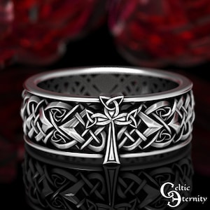 May include: A silver Celtic knot ring with a cross design. The ring is intricately detailed and has a polished finish.