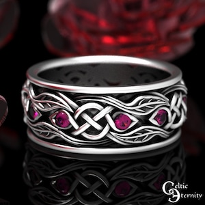 Puede incluir: Un anillo de plata con un nudo celta adornado con tres piedras preciosas rosas. El anillo es ancho y presenta detalles intrincados.