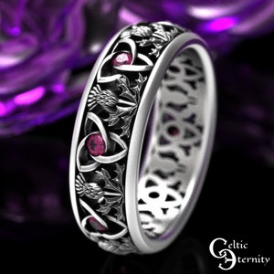 Puede incluir: Un anillo de plata con un nudo celta, un diseño de cardo y piedras preciosas rojas. El anillo es un símbolo tradicional de amor y eternidad.