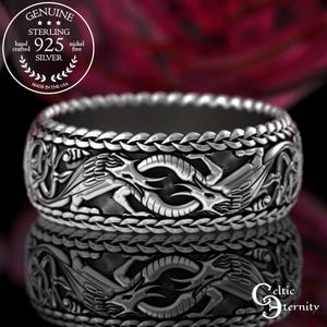 Puede incluir: Un anillo de plata de ley con un diseño detallado de dragón. El anillo presenta un borde trenzado e intrincados grabados de dragones alrededor de la banda. El anillo está marcado "925 Silver" y "Hand Crafted Made in the USA".