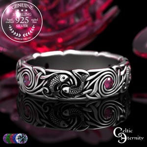 May include: A silver ring with a Celtic knot design. The ring features two fish and pink gemstones. The ring is hand crafted and nickel free. The text on the ring says "Genuine Sterling 925 Silver".