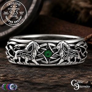May include: A sterling silver ring featuring two embossed lion figures facing each other, separated by a central green gemstone. The band displays an intricate, continuous knotwork pattern throughout, with a dark, oxidized finish highlighting the details.