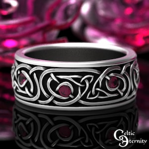 May include: A silver Celtic knot ring with three red gemstones. The ring is a wide band with a detailed knot design.