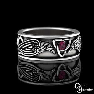 Puede incluir: Un anillo plateado con un diseño celta. El anillo presenta patrones estilizados de aves y nudos, con una gema roja engastada en un símbolo de triqueta. El anillo se muestra sobre un fondo negro.