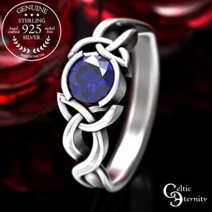 Puede incluir: Un anillo de plata de ley con un diseño de nudo celta. El anillo presenta una piedra preciosa redonda de color azul oscuro engastada en un patrón detallado e entrelazado. El anillo está marcado con "925 Silver" y "Made in the USA".