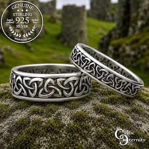 Könnte beinhalten: Zwei Ringe aus Sterlingsilber mit einem durchgehenden, geprägten Triquetra-Knotenmuster. Das Metall hat eine polierte Oberfläche mit abgedunkelten vertieften Bereichen, um das komplexe Design hervorzuheben. Ein kreisförmiges Siegel zeigt Genuine Sterling 925.