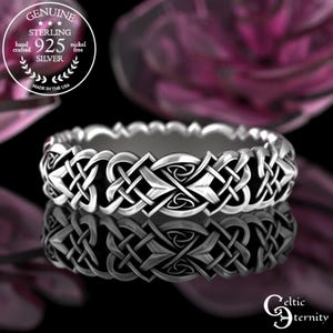 May include: A sterling silver ring with an intricate Celtic knot design. The ring is nickel-free and hand-crafted in the USA. The ring's design is reflected in the glossy black surface below. The ring is marked with "925 Silver".