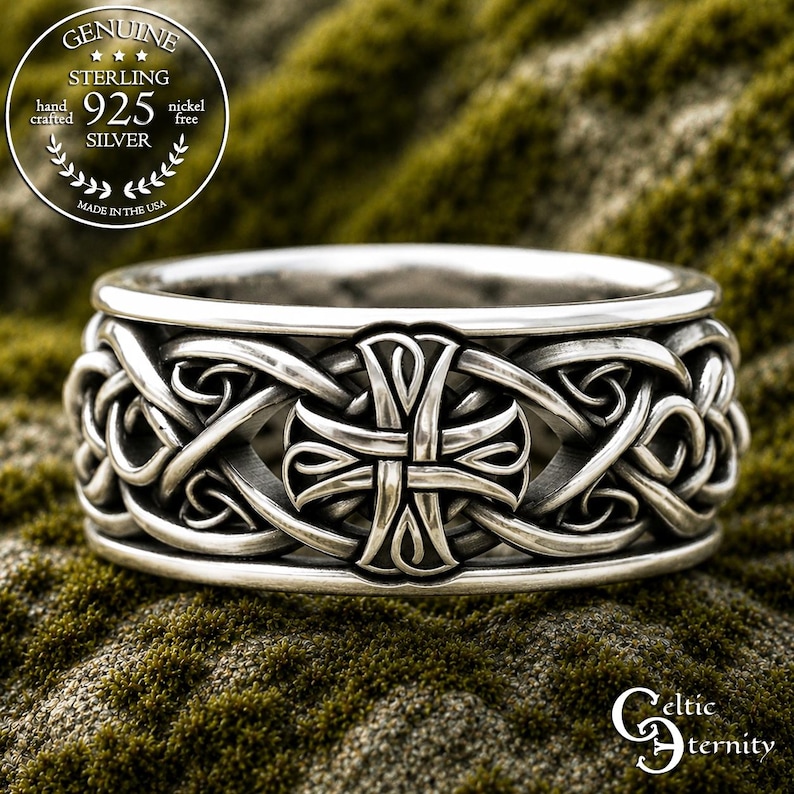 May include: A sterling silver ring featuring an intricate embossed Celtic cross design surrounded by continuous interwoven knotwork patterns. The band has a polished finish with darkened recessed areas to highlight the detailed metalwork.