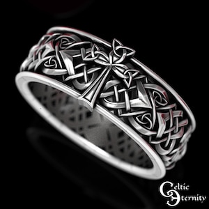 May include: A silver Celtic knot ring with a cross design. The ring is intricately detailed and features a Celtic knot pattern.