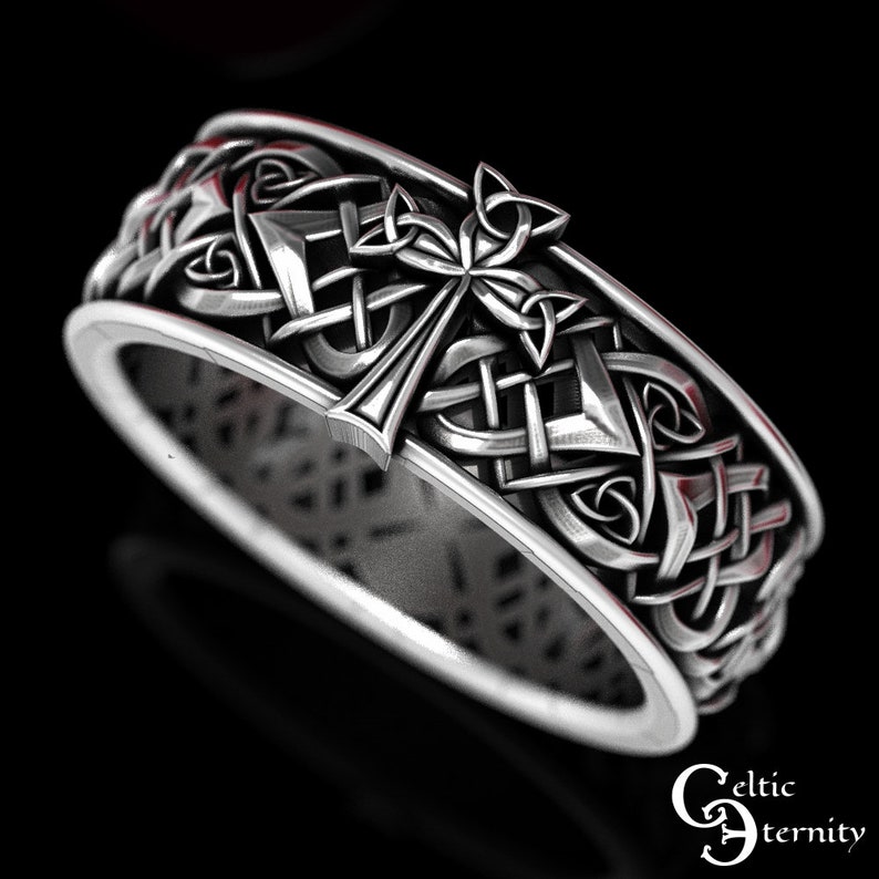 May include: A silver Celtic knot ring with a cross design. The ring is intricately detailed and features a Celtic knot pattern.