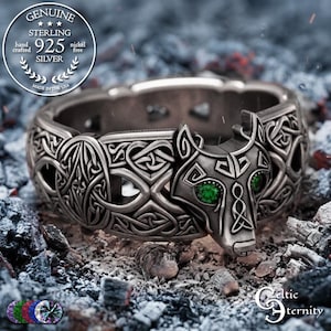 May include: A sterling silver ring featuring an intricate wolf head design with vibrant green gemstone eyes. The band is decorated with detailed Celtic knotwork patterns throughout, showcasing a dark, oxidised finish on the metal surface.