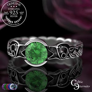 May include: A sterling silver ring with a large, round, emerald-green gemstone. The ring features a Celtic knot design and is stamped with "925 Silver" and "Made in the USA". The ring is nickel-free and hand-crafted.