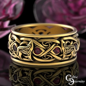 May include: A gold Celtic knot ring with a wolf design and red gemstones. The ring is a wide band with intricate details.