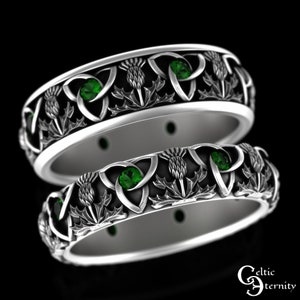 Könnte beinhalten: Zwei silberne Ringe mit keltischen Knoten, grünen Edelsteinen und Distelmotiven.
