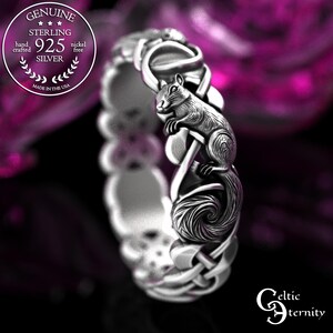 May include: A sterling silver ring featuring a detailed squirrel figure integrated into a continuous band with intricate knotwork patterns. The metal surface has a polished finish with darkened recessed areas to highlight the texture of the squirrel.