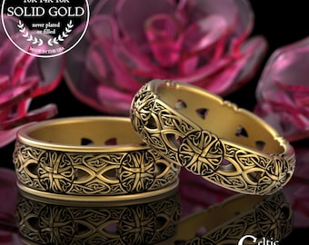 May include: Two gold rings featuring detailed Celtic knot patterns. The rings are set against a blurred floral backdrop and reflected on a surface. The rings are marked as "GENUINE SOLID GOLD" and "MADE IN THE USA". The rings are from "Celtic Eternity".