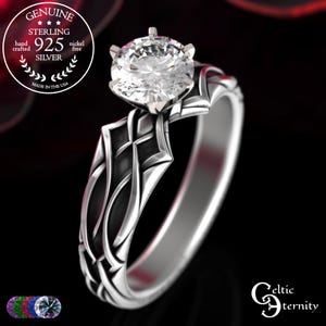 May include: A sterling silver ring with a large, clear gemstone. The ring features an intricate Celtic knot design on the band and setting. The image includes text that reads "Genuine Sterling 925 Silver" and "Made in the USA."