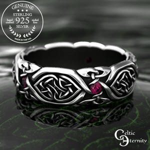 Puede incluir: Anillo de plata de ley con diseño de nudo celta y piedras rojas incrustadas. El anillo está hecho a mano y no contiene níquel. El texto de la imagen dice "Genuine Sterling 925 Silver" y "Made in the USA".