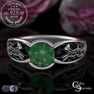 Puede incluir: Un anillo de plata de ley con una gema redonda de color verde esmeralda en el centro. La banda presenta intrincados diseños de nudos celtas a cada lado. El anillo no contiene níquel y está hecho a mano en los EE. UU. El texto "Celtic Eternity" es visible.