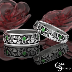 Könnte beinhalten: Zwei silberne keltische Knoten-Eheringe mit grünen Edelsteinen. Die Ringe haben ein dreifaches Knotendesign mit einem gekrönten Herzen in jedem Knoten.