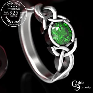 Puede incluir: Un anillo de plata de ley con un diseño de nudo celta. El anillo presenta una piedra preciosa verde redonda y brillante. La banda está pulida y el anillo está sobre un fondo negro. Hecho a mano y sin níquel.