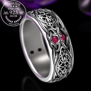 Puede incluir: Un anillo de plata con un diseño de nudo celta y dos piedras preciosas rojas. El anillo está hecho de plata de ley y es libre de níquel.