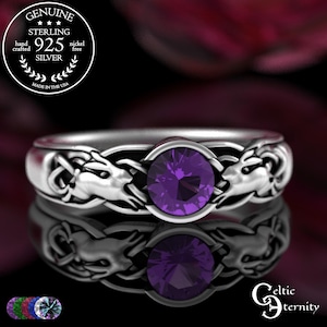 May include: A sterling silver ring with a purple gemstone center. The ring features a Celtic knot design with two animal heads on the sides. The ring is marked "925 Silver" and "Made in the USA". The ring is nickel free.
