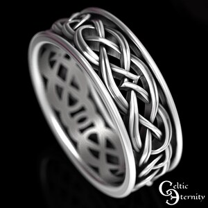 May include: A silver-toned metal ring featuring an intricate, continuous woven knot pattern around the outer band. The design includes a smooth, raised border on both edges. The text "Celtic Eternity" is visible in the bottom right corner.