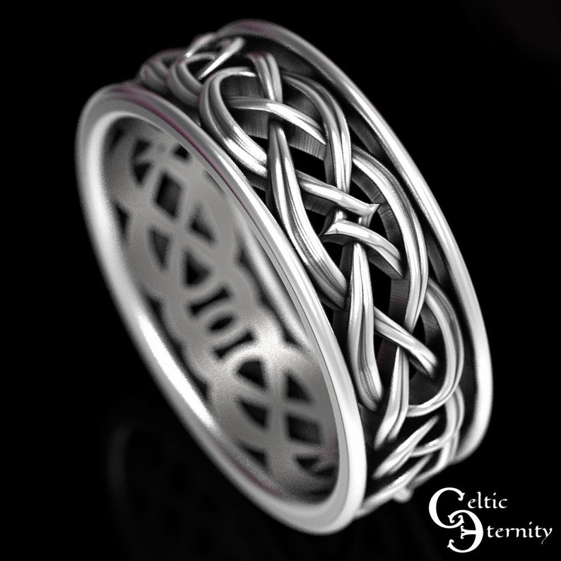 May include: A silver-toned metal ring featuring an intricate, continuous woven knot pattern around the outer band. The design includes a smooth, raised border on both edges. The text "Celtic Eternity" is visible in the bottom right corner.